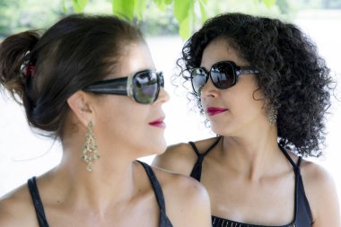 Arka planda ağaçlar olan bir nehre karşı güneş gözlüğü takan iki kız kardeşin portresi. Salvador, Bahia, Brezilya.