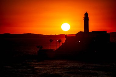 Salvador, Bahia, Brezilya - 19 Eylül 2021: Brezilya 'nın Bahia eyaletindeki Barra plajında güzel ve dramatik bir turuncu gün batımına karşı bir deniz fenerinin silueti.