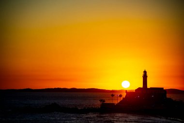 Salvador, Bahia, Brezilya - 19 Eylül 2021: Brezilya 'nın Bahia eyaletindeki Barra plajında güzel ve dramatik bir turuncu gün batımına karşı bir deniz fenerinin silueti.