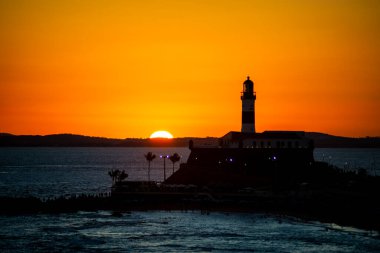 Salvador, Bahia, Brezilya - 19 Eylül 2021: Brezilya 'nın Bahia eyaletindeki Barra plajında güzel ve dramatik bir turuncu gün batımına karşı bir deniz fenerinin silueti.