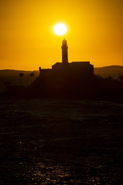 Salvador, Bahia, Brezilya - 19 Eylül 2021: Brezilya 'nın Bahia eyaletindeki Barra plajında güzel ve dramatik bir turuncu gün batımına karşı bir deniz fenerinin silueti.
