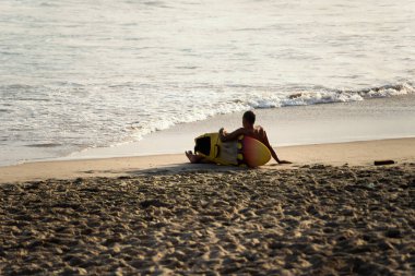 Salvador, Bahia, Brezilya - 26 Eylül 2021: Sahilde oturmuş denize bakan sörfçü. Farol da Barra plajı Salvador, Bahia eyaleti, Brezilya.