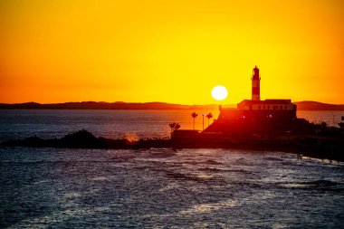 Salvador, Bahia, Brezilya - 19 Eylül 2021: Brezilya 'nın Bahia eyaletindeki Barra plajında güzel ve dramatik bir turuncu gün batımına karşı bir deniz fenerinin silueti.