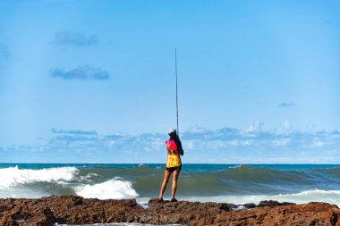 Salvador, Bahia, Brezilya - 10 Ekim 2021: Brezilya 'nın Bahia kentinin başkenti Salvador' da Rio Vermelho 'da kayalıklarda balık tutan balıkçı kadın