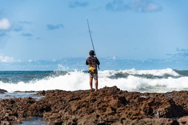 Salvador, Bahia, Brezilya - 10 Ekim 2021 Rio Vermelho sahilindeki kayalıklarda balık tutan erkekler sırıkla, Bahia, Brezilya 'nın başkenti Salvador' da balık tutuyorlar.