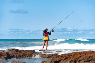 Salvador, Bahia, Brezilya - 10 Ekim 2021: Brezilya 'nın Bahia kentinin başkenti Salvador' da Rio Vermelho 'da kayalıklarda balık tutan balıkçı kadın