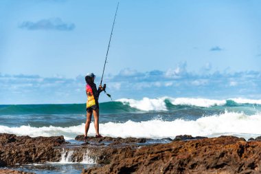 Salvador, Bahia, Brezilya - 10 Ekim 2021: Brezilya 'nın Bahia kentinin başkenti Salvador' da Rio Vermelho 'da kayalıklarda balık tutan balıkçı kadın