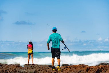Salvador, Bahia, Brezilya - 10 Ekim 2021: Erkek ve kadın balıkçılar balık oltasıyla kayaların tepesinde. Salvador şehri, Bahia 'nın başkenti, Brezilya
