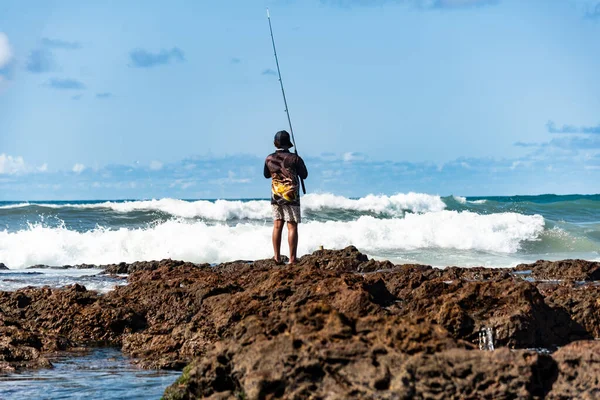 Salvador, Bahia, Brezilya - 10 Ekim 2021 Rio Vermelho sahilindeki kayalıklarda balık tutan erkekler sırıkla, Bahia, Brezilya 'nın başkenti Salvador' da balık tutuyorlar.