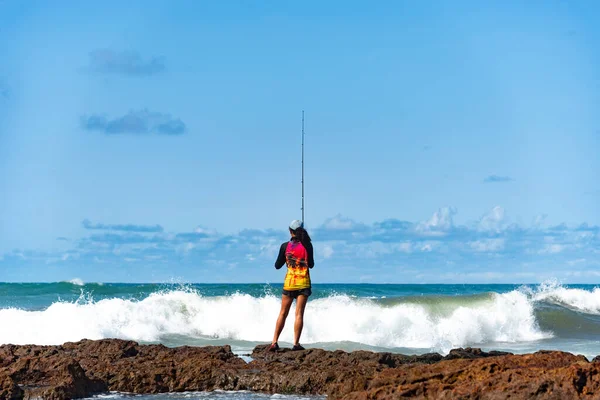 Salvador, Bahia, Brezilya - 10 Ekim 2021: Brezilya 'nın Bahia kentinin başkenti Salvador' da Rio Vermelho 'da kayalıklarda balık tutan balıkçı kadın