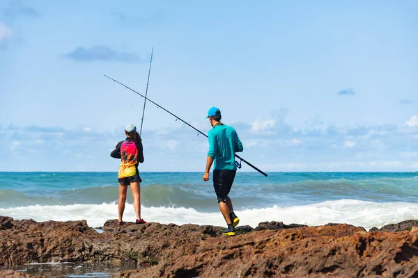 Salvador, Bahia, Brezilya - 10 Ekim 2021: Erkek ve kadın balıkçılar balık oltasıyla kayaların tepesinde. Salvador şehri, Bahia 'nın başkenti, Brezilya