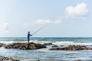 Salvador, Bahia, Brezilya - 10 Ekim 2021: Bahia, Brezilya 'nın başkenti Salvador' da Boca do Rio plajında kayalıklarda balık tutan balıkçı