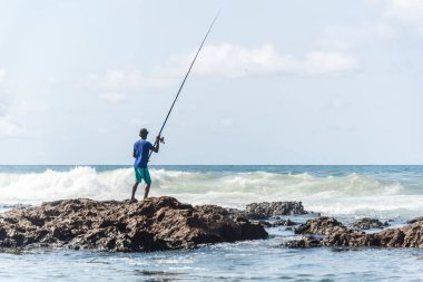 Salvador, Bahia, Brezilya - 10 Ekim 2021: Bahia, Brezilya 'nın başkenti Salvador' da Boca do Rio plajında kayalıklarda balık tutan balıkçı