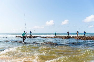 Salvador, Bahia, Brezilya - 10 Ekim 2021: Brezilya 'nın Bahia kentinin başkenti Salvador' da Boca do Rio plajında kayalıklarda balık tutan balıkçılar