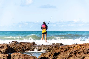 Salvador, Bahia, Brezilya - 10 Ekim 2021: Brezilya 'nın Bahia kentinin başkenti Salvador' da Rio Vermelho 'da kayalıklarda balık tutan balıkçı kadın