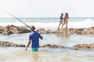 Salvador, Bahia, Brezilya - 10 Ekim 2021: Brezilya 'nın Bahia kentinin başkenti Salvador' da Boca do Rio plajında kayalıklarda balık tutan balıkçılar