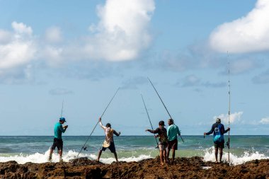 Salvador, Bahia, Brezilya - 10 Ekim 2021: Brezilya 'nın Bahia kentinin başkenti Salvador' da Boca do Rio plajında kayalıklarda balık tutan balıkçılar