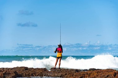 Salvador, Bahia, Brezilya - 10 Ekim 2021: Brezilya 'nın Bahia kentinin başkenti Salvador' da Rio Vermelho 'da kayalıklarda balık tutan balıkçı kadın
