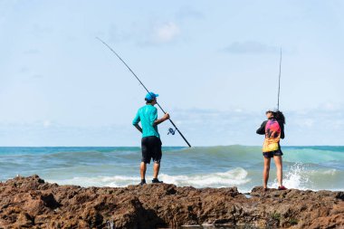 Salvador, Bahia, Brezilya - 10 Ekim 2021: Erkek ve kadın balıkçılar balık oltasıyla kayaların tepesinde. Salvador şehri, Bahia 'nın başkenti, Brezilya
