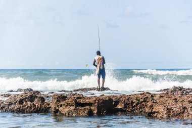 Salvador, Bahia, Brezilya - 10 Ekim 2021: Bahia, Brezilya 'nın başkenti Salvador' da Boca do Rio plajında kayalıklarda balık tutan balıkçı