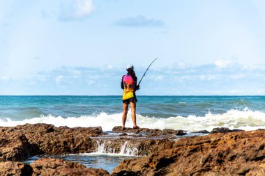 Salvador, Bahia, Brezilya - 10 Ekim 2021: Brezilya 'nın Bahia kentinin başkenti Salvador' da Rio Vermelho 'da kayalıklarda balık tutan balıkçı kadın