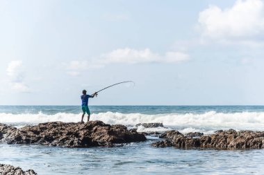 Salvador, Bahia, Brezilya - 10 Ekim 2021: Bahia, Brezilya 'nın başkenti Salvador' da Boca do Rio plajında kayalıklarda balık tutan balıkçı
