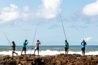 Salvador, Bahia, Brezilya - 10 Ekim 2021: Brezilya 'nın Bahia kentinin başkenti Salvador' da Boca do Rio plajında kayalıklarda balık tutan balıkçılar