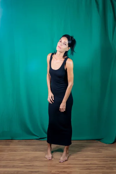 Portrait of standing adult model in black dress against dark green background. Salvador, Bahia, Brazil.