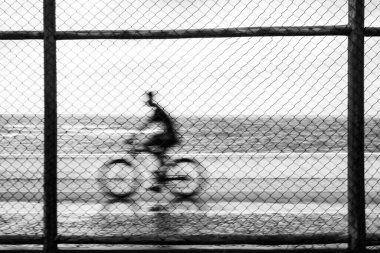 Yağmur sırasında spor çitlerinin arkasından geçen bisikletçi siluetleri. Salvador, Bahia, Brezilya.