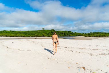 Young beautiful woman walking on the beach sand towards the trees and the mangrove. Praia do Guaibim, coast of the sea of Bahia, Brazil