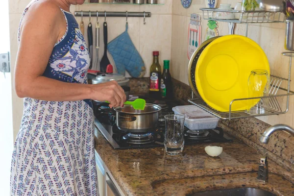 Young woman making food in pan with green plastic spatula.