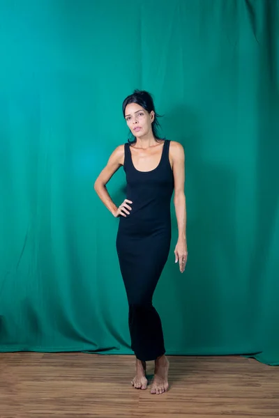 Portrait of standing adult model in black dress against dark green background. Salvador, Bahia, Brazil.