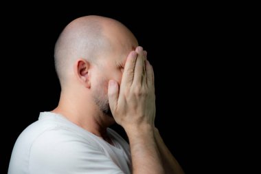 Siyah arka planda elleri yüzünde olan kel bir adamın portresi. Salvador, Bahia, Brezilya.