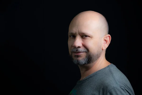 Portrait of a bald bearded man looking at the camera against a black background. Salvador, Bahia, Brazil.