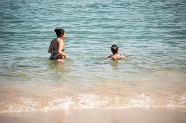 Anne ve kız bikinili olarak Salvador, Bahia 'daki Porto da Barra plajına giriyor..