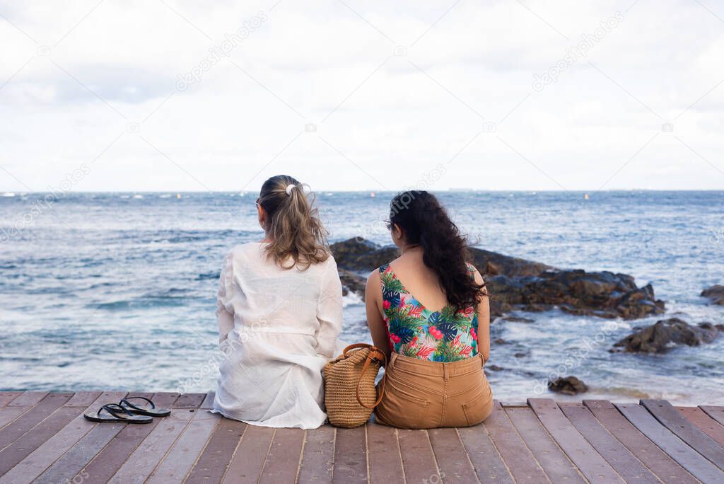 Mother and daughter sitting on the pier of the port of Barra facing the sea. Salvador, Bahia, Brazil.