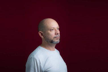 Portrait of a bald bearded man looking up against a red background. Salvador, Bahia, Brazil.