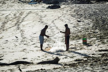 Salvador, Bahia, Brazil - November 01, 2021: Two fishermen collecting fishing net with fish on the beach of Rio Vermelho in Salvador, Bahia.