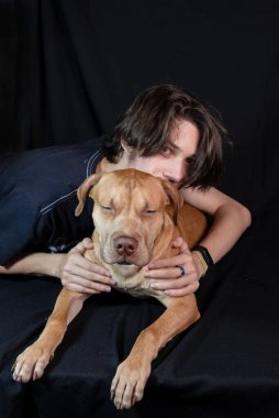 Siyah arka planda karamel renkli pitbull köpeği olan genç bir adamın portresi. Salvador, Bahia, Brezilya.