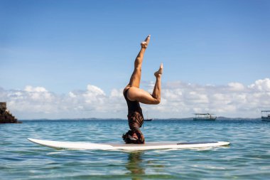 Salvador, Bahia, Brazil - June 04, 2022: Woman stands upside down on a surfboard at Porto da Barra beach in Salvador, Bahia.