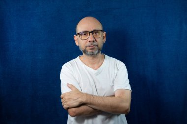 Portrait of a bearded bald man against blue background.