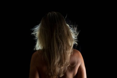 Portrait of a Shirtless Woman Back to the Camera Against Black Background. artistic nude.