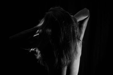 Portrait of a Shirtless Woman Back to the Camera Against Black Background. artistic nude.