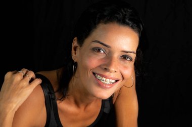 Studio portrait of young woman in black t-shirt smiling at camera against black studio background. Salvador, Brazil.