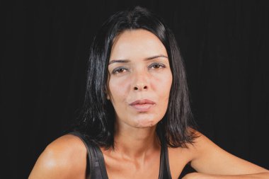 Studio portrait of young woman looking at camera against simple studio black background. She wears a black t-shirt.