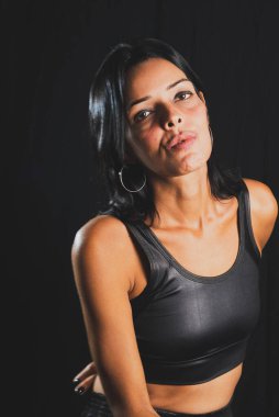 Studio portrait of young woman looking at camera against simple studio black background. She wears a black t-shirt.