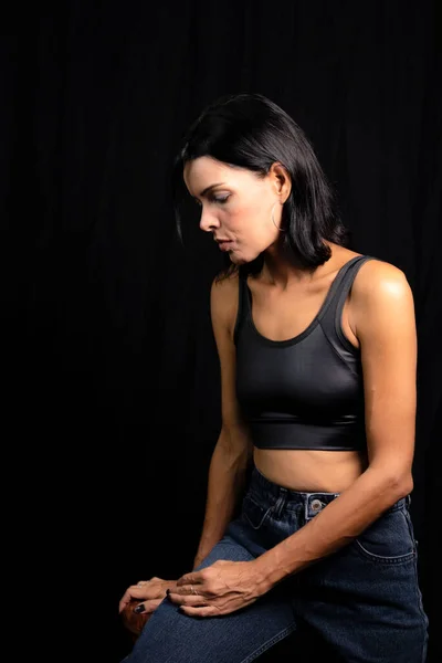 Studio portrait of young woman in black t-shirt against plain black studio background. She standing in the studio.