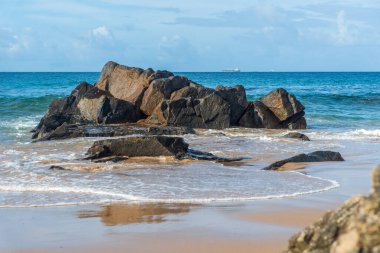 A wave breaks about a rock during a curtain on the sea. Farol da Barra beach, Salvador, Brazil.