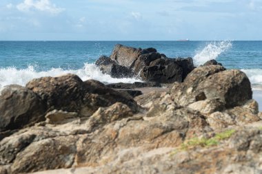 A wave breaks about a rock during a curtain on the sea. Farol da Barra beach, Salvador, Brazil.