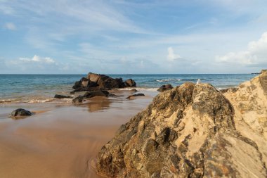 A wave breaks about a rock during a curtain on the sea. Farol da Barra beach, Salvador, Brazil.